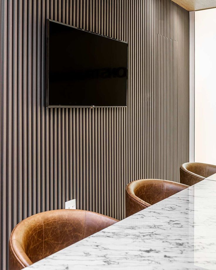 a television mounted on the wall in a room with leather chairs and marble counter tops