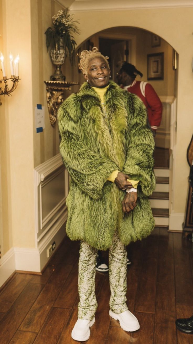 a woman in a green fur coat and white shoes standing on a wooden floor next to a doorway