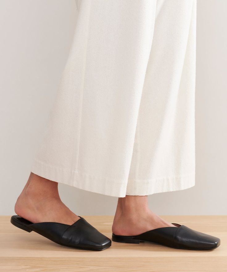 a woman in white pants and black shoes standing on a wooden floor with her legs crossed