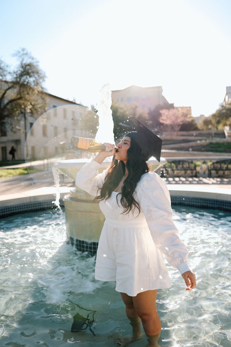 a woman standing in front of a fountain drinking from a bottle