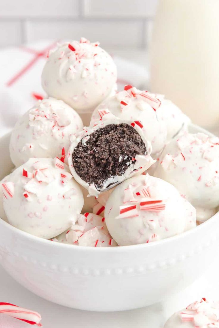 a bowl filled with white chocolate peppermint truffles next to a glass of milk