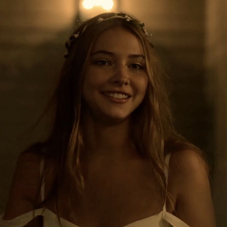 a woman with long hair wearing a white dress and flower crown smiling at the camera