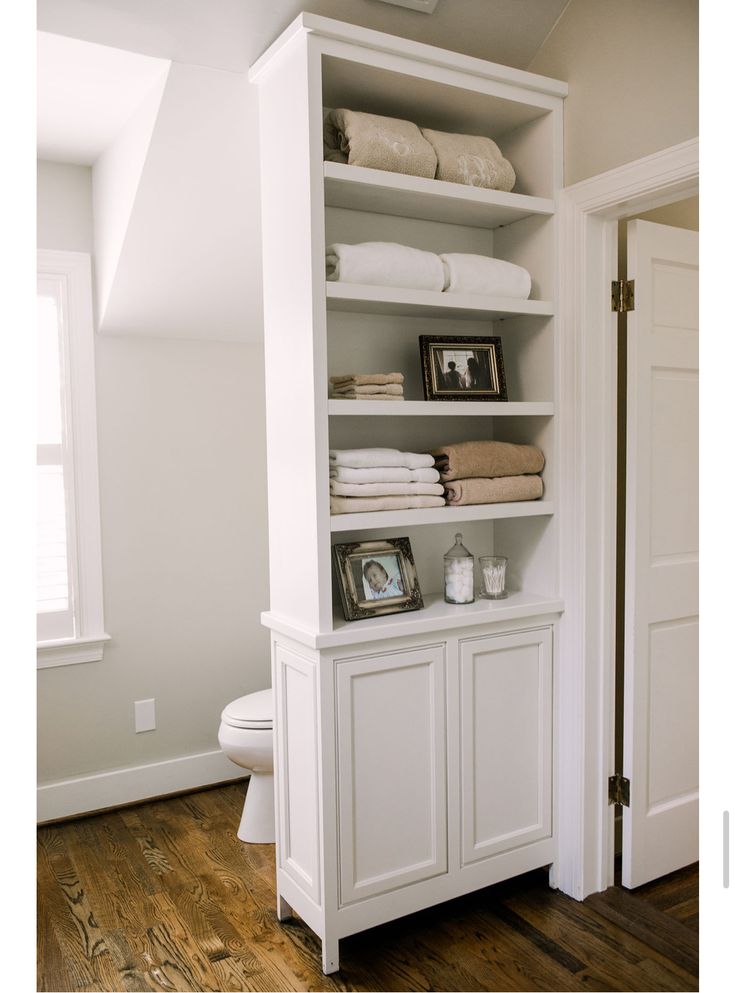 a bathroom with white cabinets and towels on top of the shelves in front of the toilet