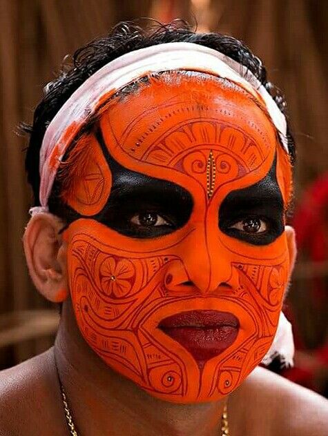 a woman with orange face paint on her face and headdress, looking at the camera