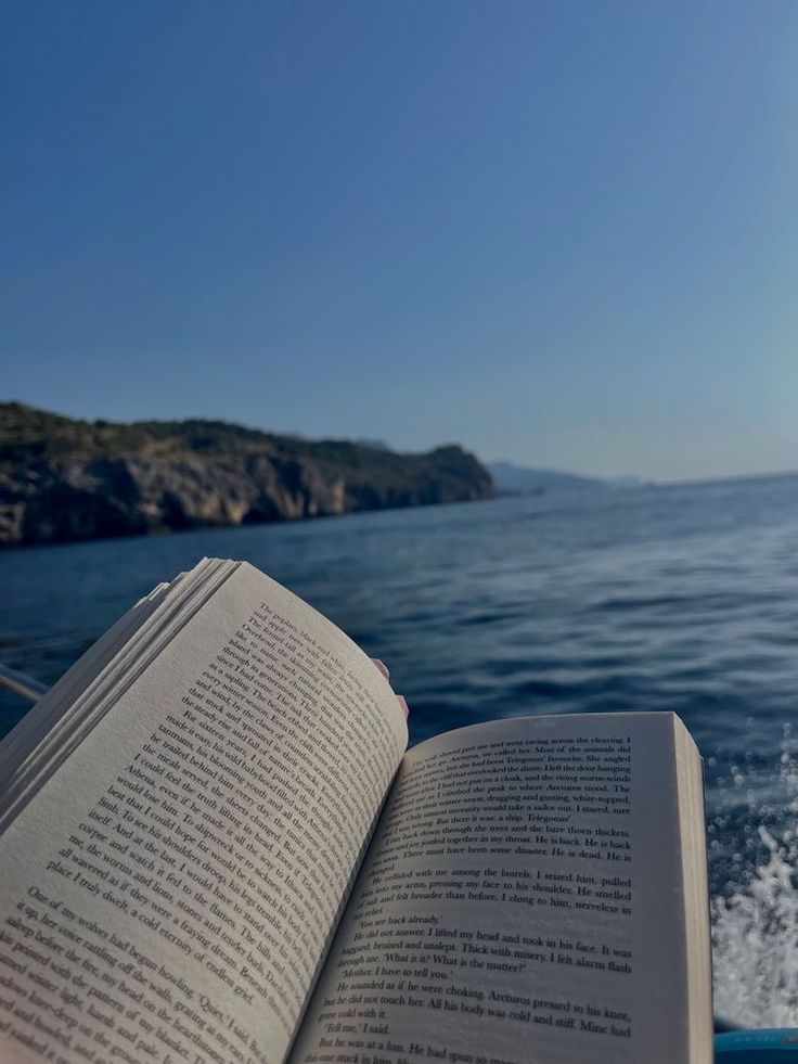 an open book sitting on top of a boat in the ocean next to a cliff