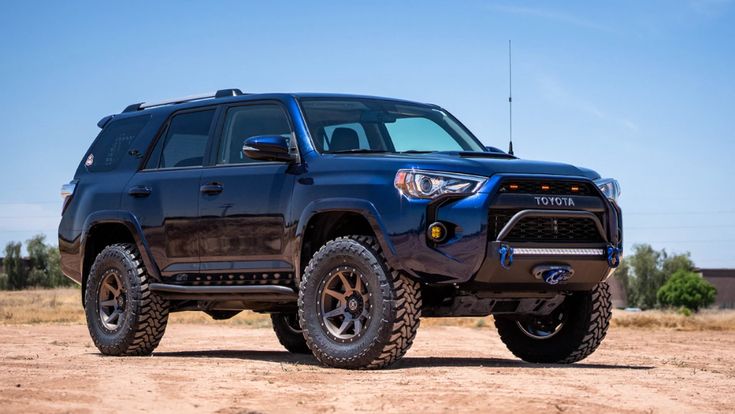 the front end of a blue toyota 4runner on dirt road with sky in background