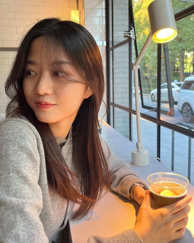 a woman sitting at a table with a cup of tea in her hand and looking into the camera