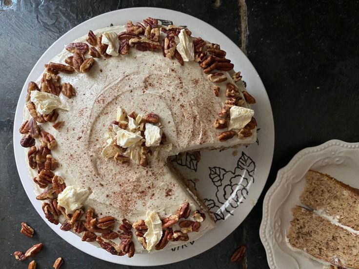 a white plate topped with a cake covered in pecans next to a slice of cake