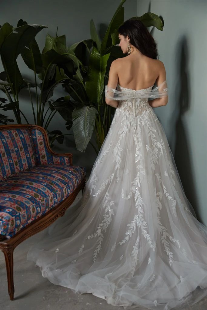 a woman in a white wedding dress standing next to a couch and looking at the wall