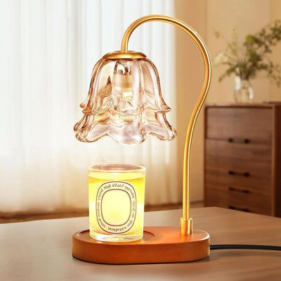 a glass lamp on a wooden table with a candle in front of it and a window behind it