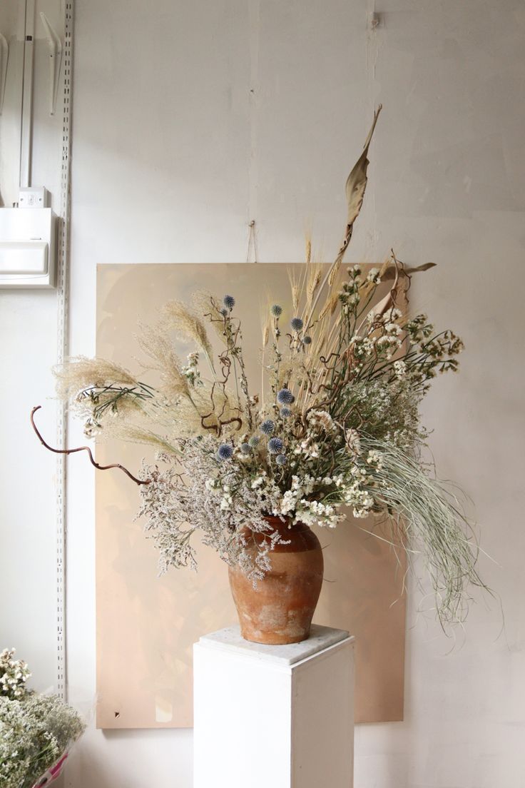 a vase filled with lots of flowers sitting on top of a white pedestal next to a mirror