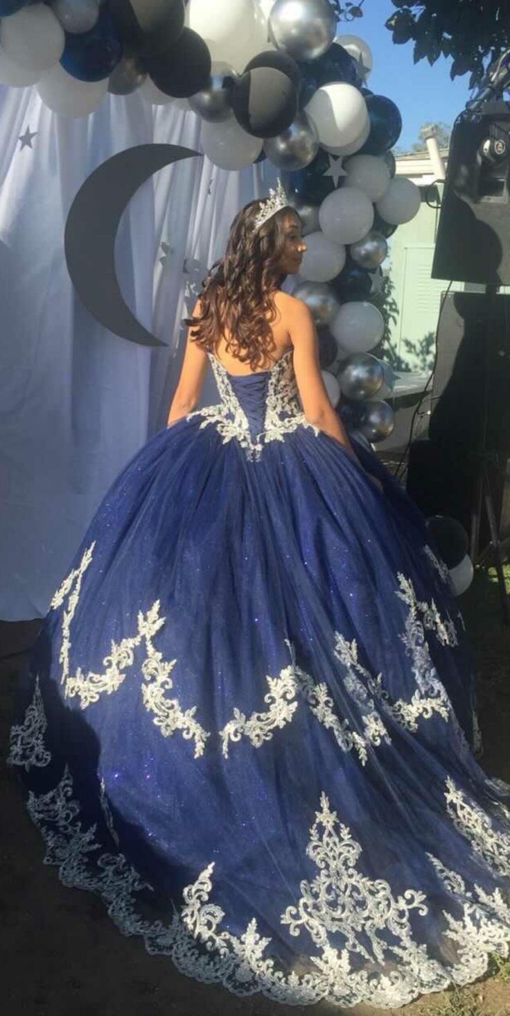 a woman in a blue and white ball gown standing under an arch decorated with balloons