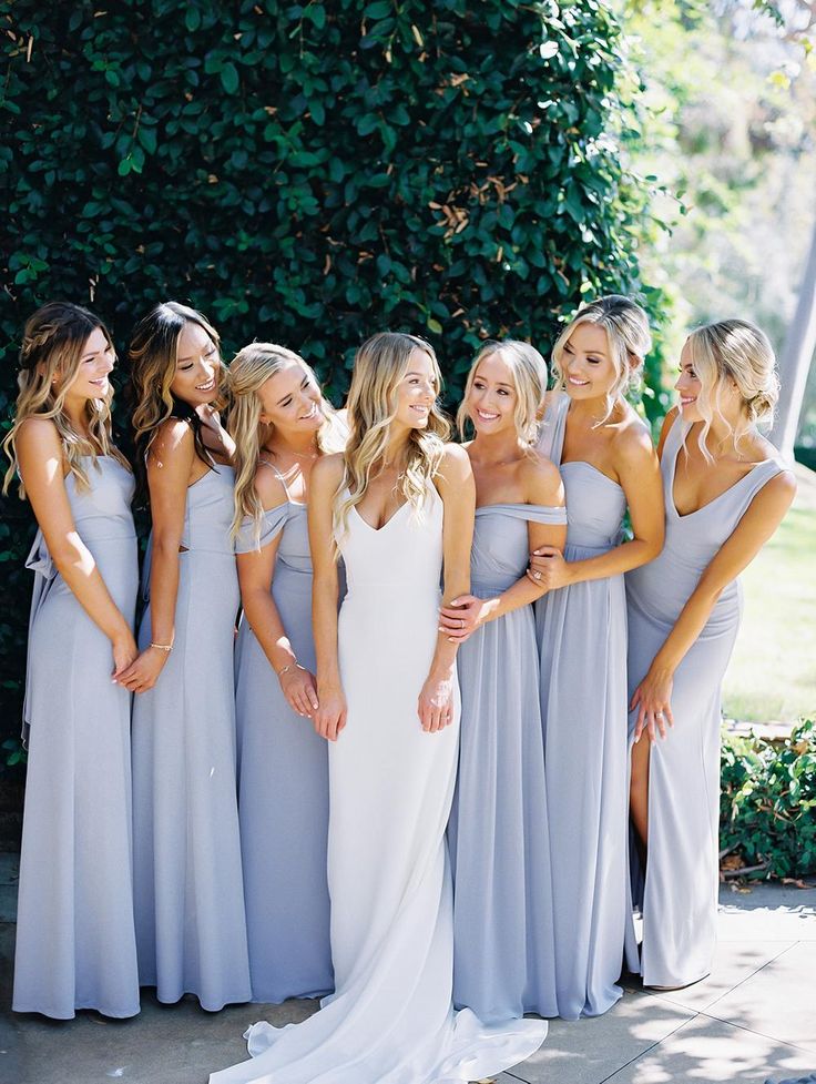 a group of women standing next to each other in long gray dresses and one woman wearing a white dress