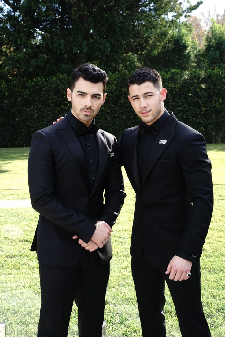 two men in tuxedos standing next to each other on a grass covered field