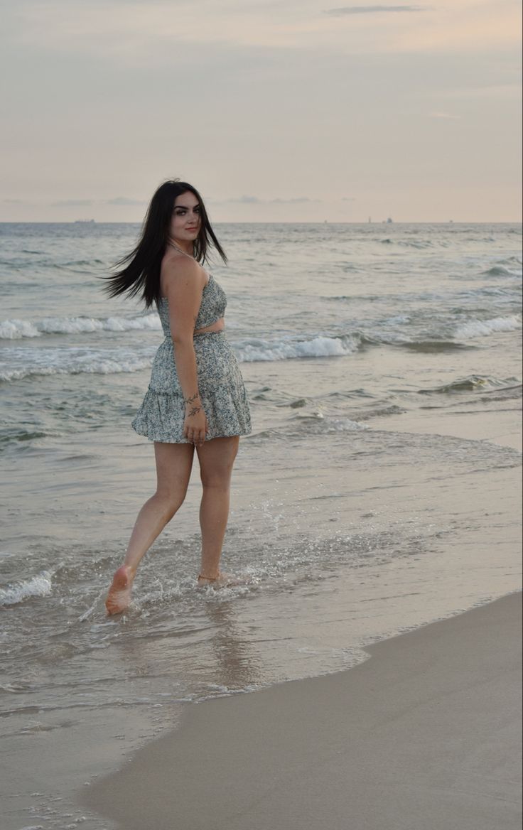 a woman standing on top of a sandy beach next to the ocean with her feet in the water