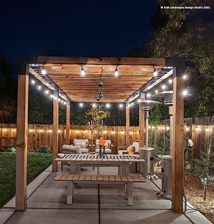 an outdoor dining area with lights on the pergolated roof and wooden benches in the foreground