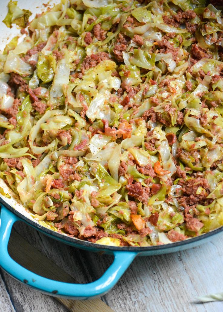 a blue skillet filled with cabbage, meat and cheese on top of a wooden table