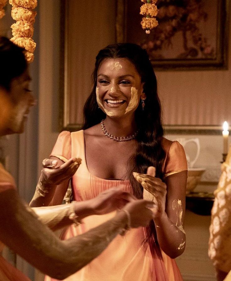 a woman in an orange dress smiles as another man holds something up to her face