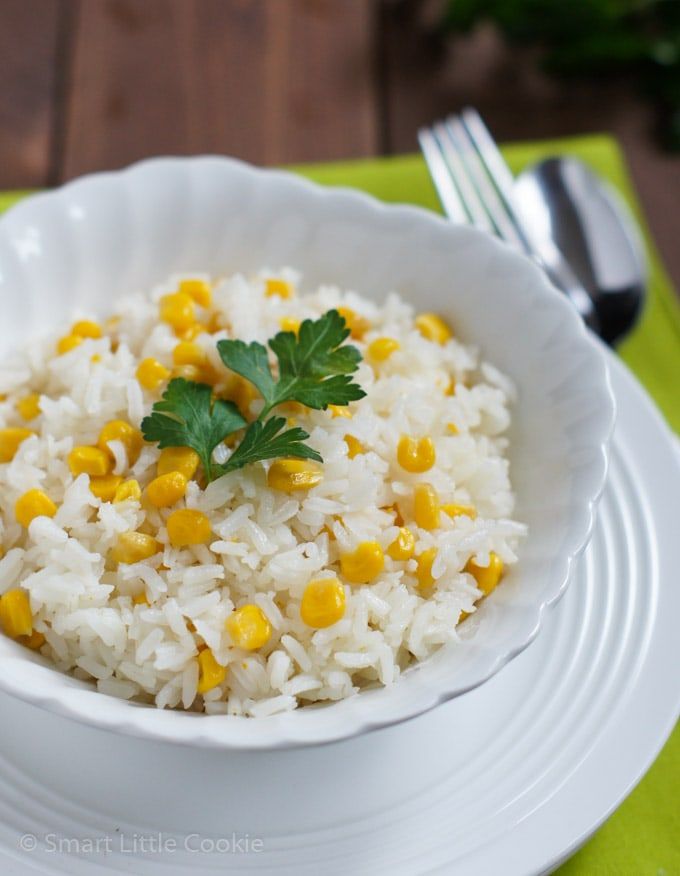 a white bowl filled with rice and corn on top of a green place mat next to a fork