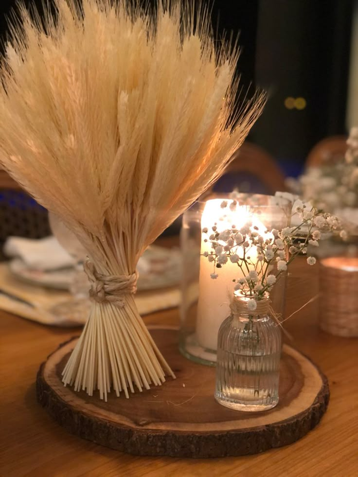 two vases with dried flowers and candles on a wooden table in front of a mirror