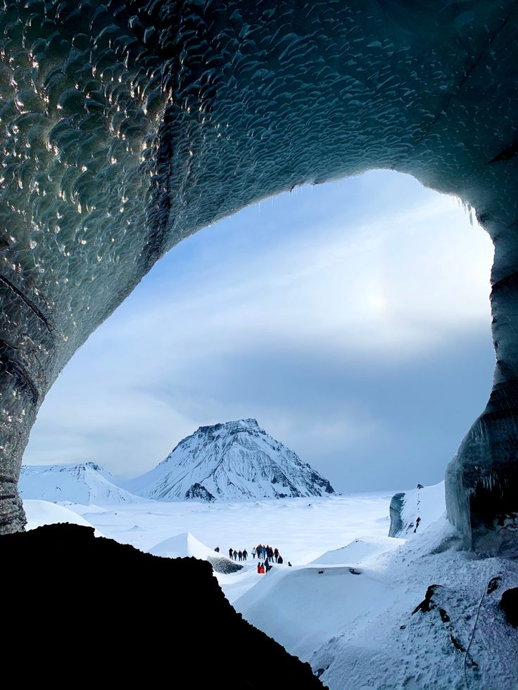 the inside of an ice cave with people standing in it and mountains in the background