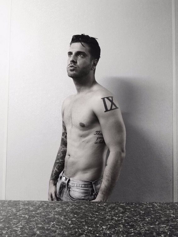 a shirtless man standing in front of a wall with the letter k tattooed on his chest