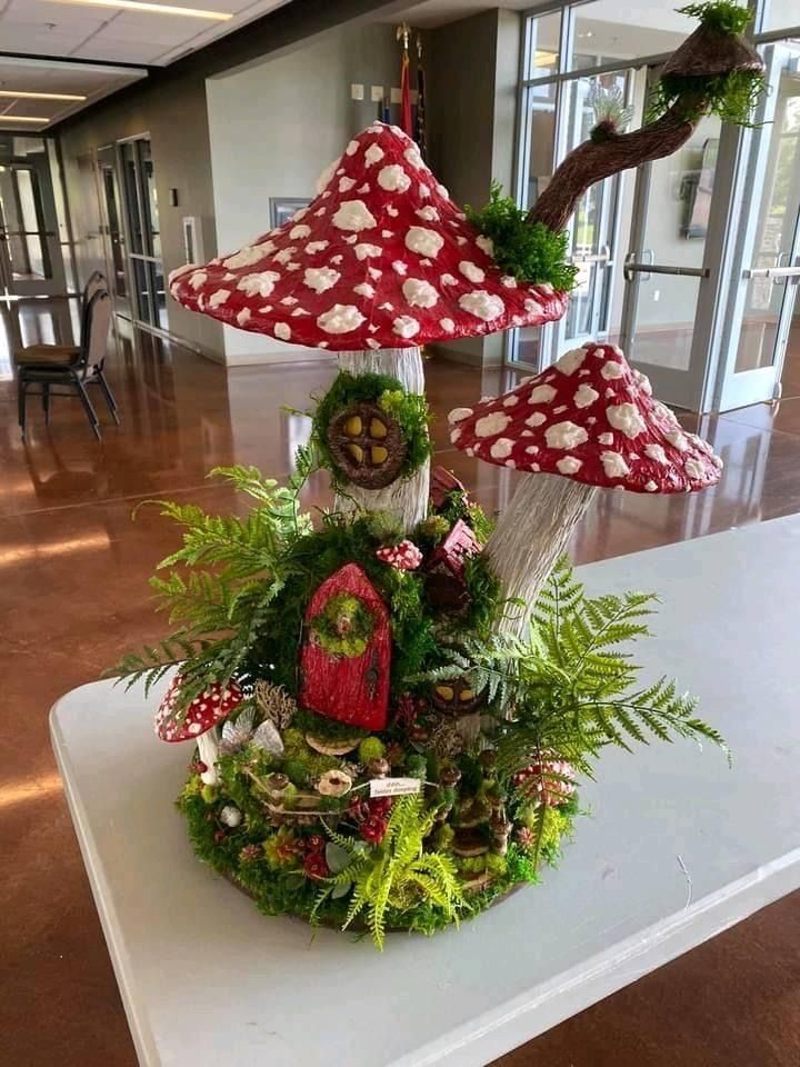 an arrangement of mushrooms and plants on a table in the middle of a room with large windows