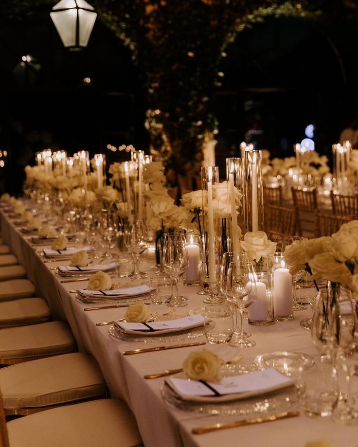 a long table is set with white flowers and candles for an elegant wedding reception at night