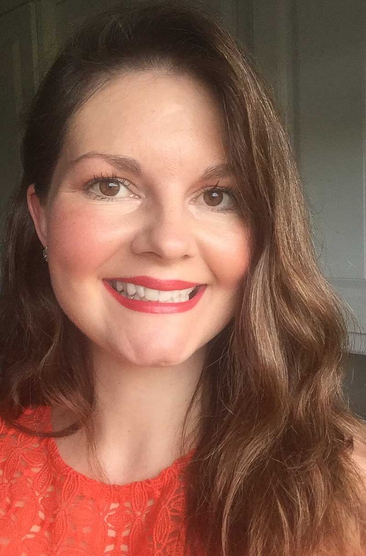 a woman in an orange top smiling at the camera with long brown hair and blue eyes