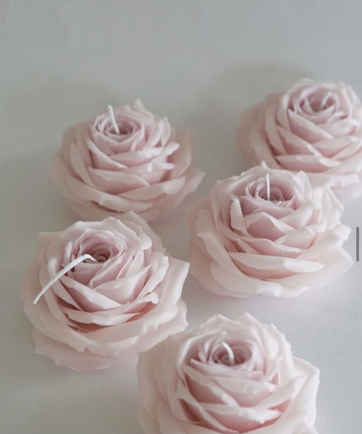 four pink roses sitting on top of a white table next to each other with string