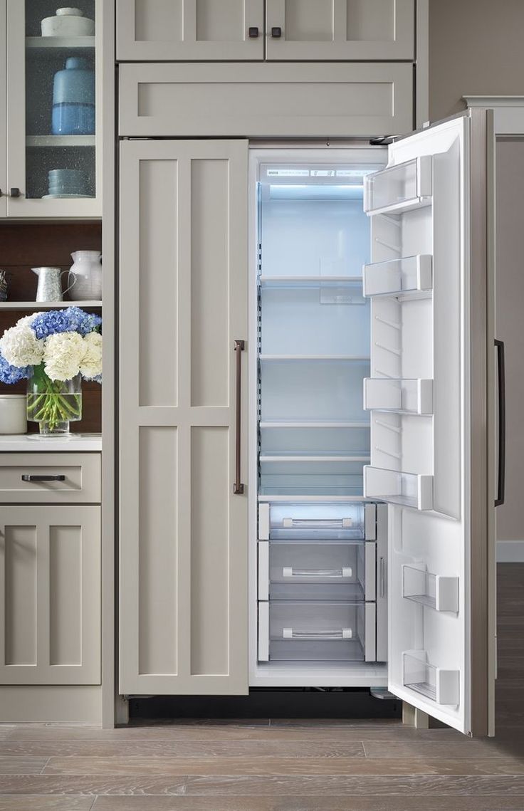 an open refrigerator door in a kitchen with white cupboards and drawers on both sides