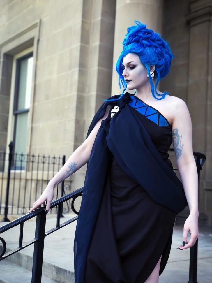 a woman with blue hair wearing a black dress and posing on the steps in front of a building