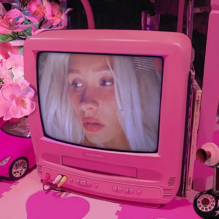 a pink television set with a woman's face on it and flowers in the background