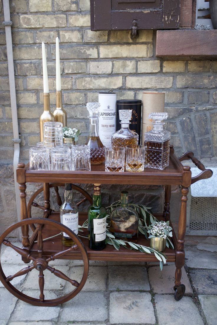 an old fashioned bar cart with liquor bottles and glasses on it next to a brick wall