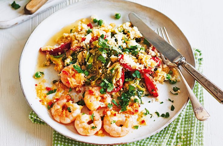 a white plate topped with shrimp and rice next to a fork on a green napkin