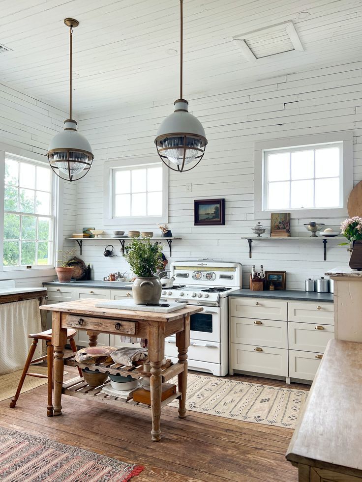 a kitchen with white walls and wooden floors, two pendant lights over the stove top