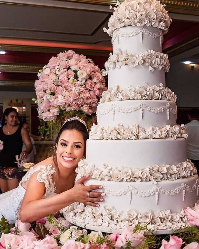 a bride and groom pose next to a large wedding cake with flowers on the table