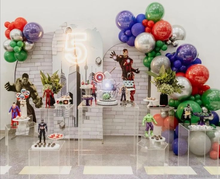 a room filled with lots of balloons and figurines on top of tables in front of a white brick wall