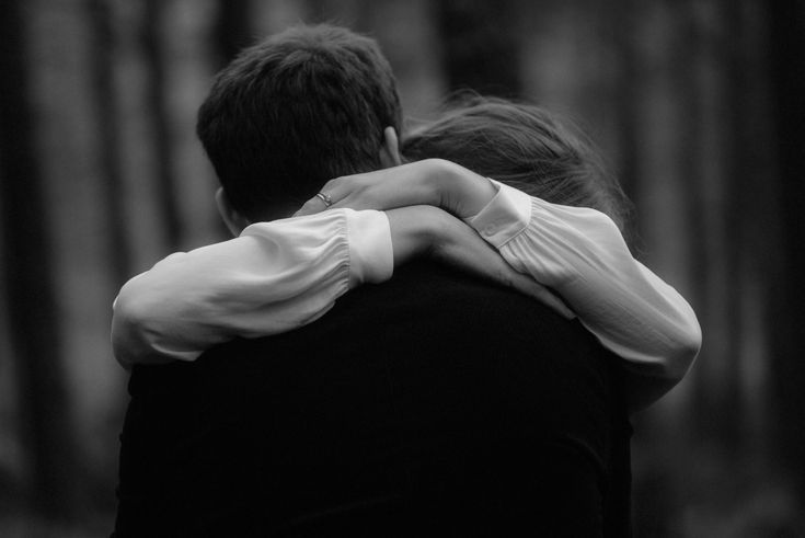 black and white photograph of two people hugging each other in front of some trees with their backs to the camera