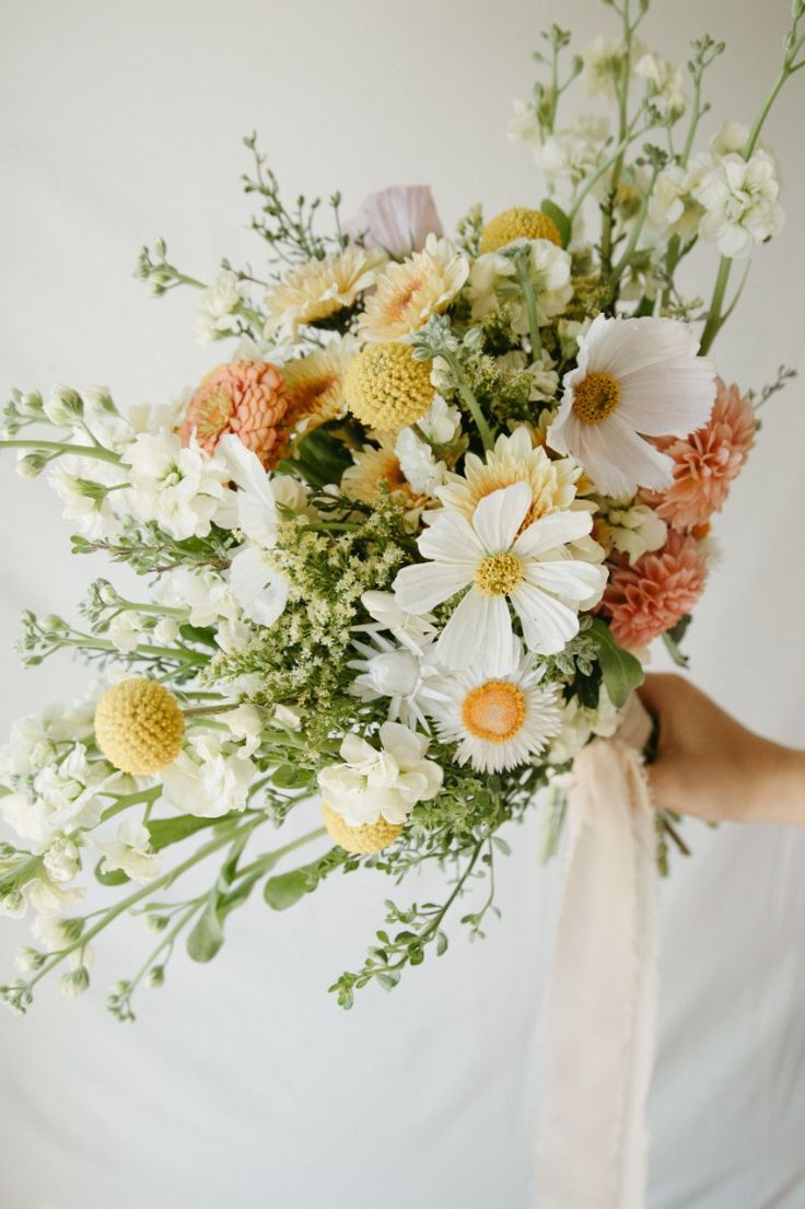 a woman holding a bouquet of white and yellow flowers in her hand with a ribbon around it