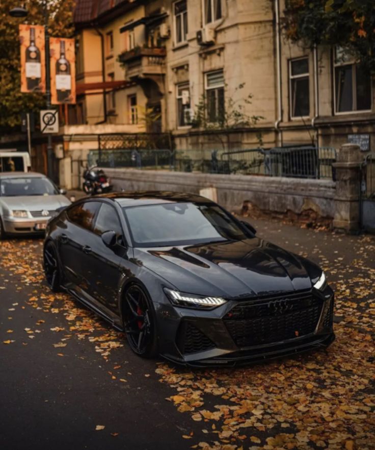 a black sports car parked on the side of a road with leaves all over it