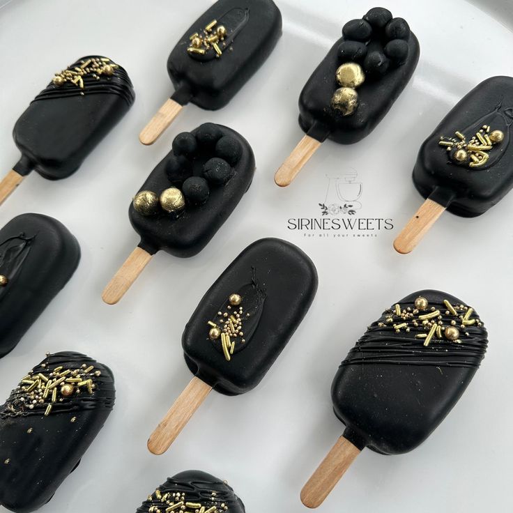 black and gold ice cream pops are arranged on a white platter with golden decorations