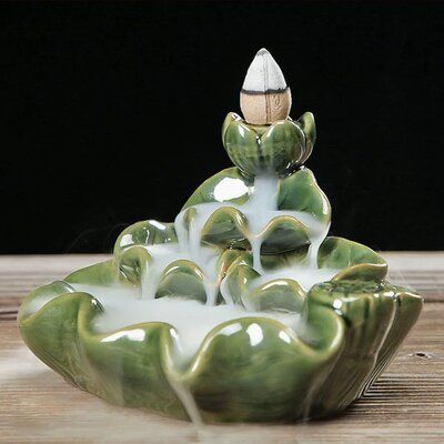 a green and white ceramic fountain with water pouring out of it's sides on a wooden table