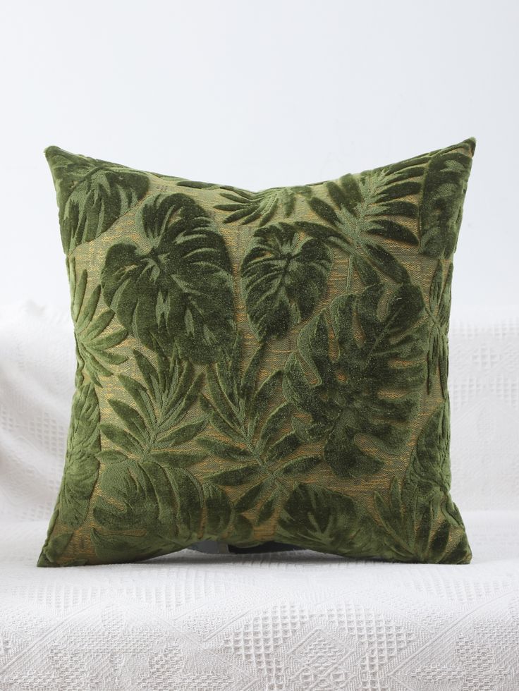 a green pillow with leaves on it sitting on top of a white bedding sheet