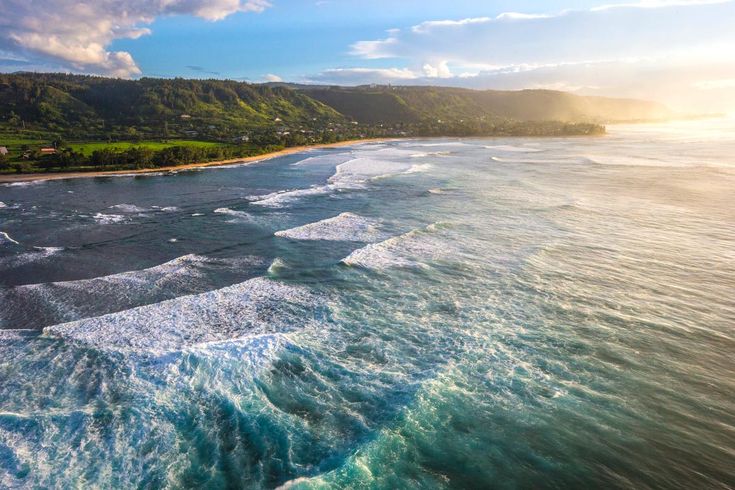 an aerial view of the ocean with waves coming in to shore and mountains in the distance