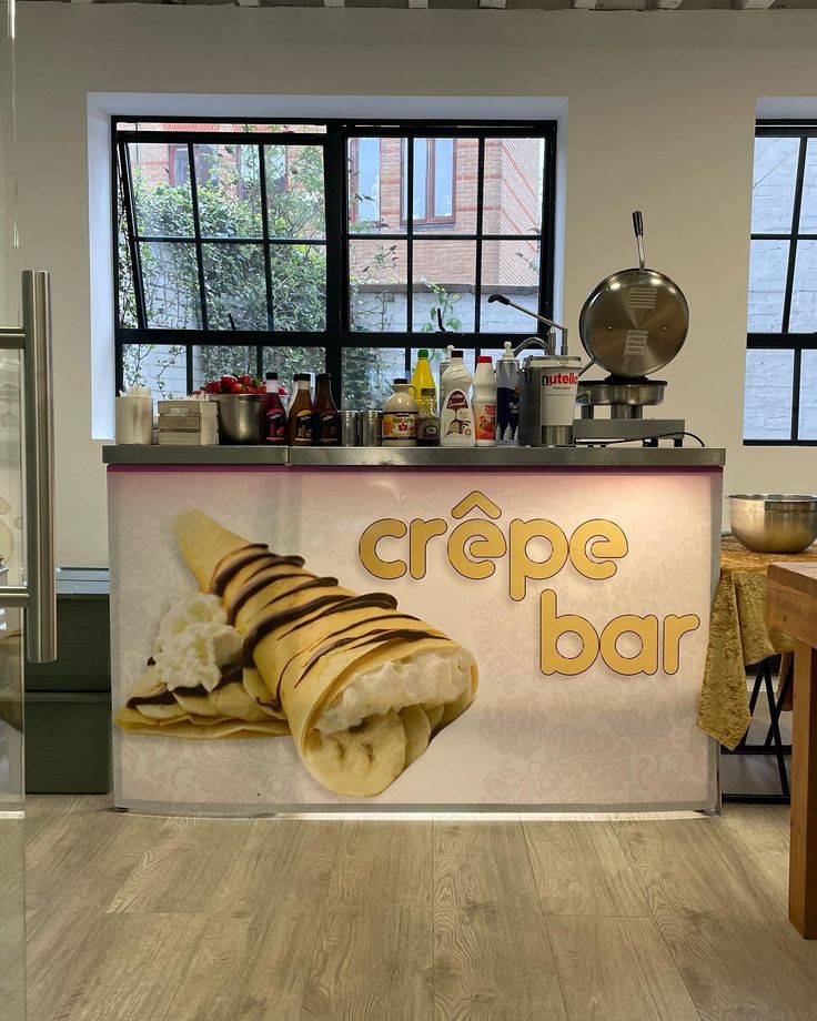 a counter that has some food on it in front of two large windows and a sign reading crepe bar