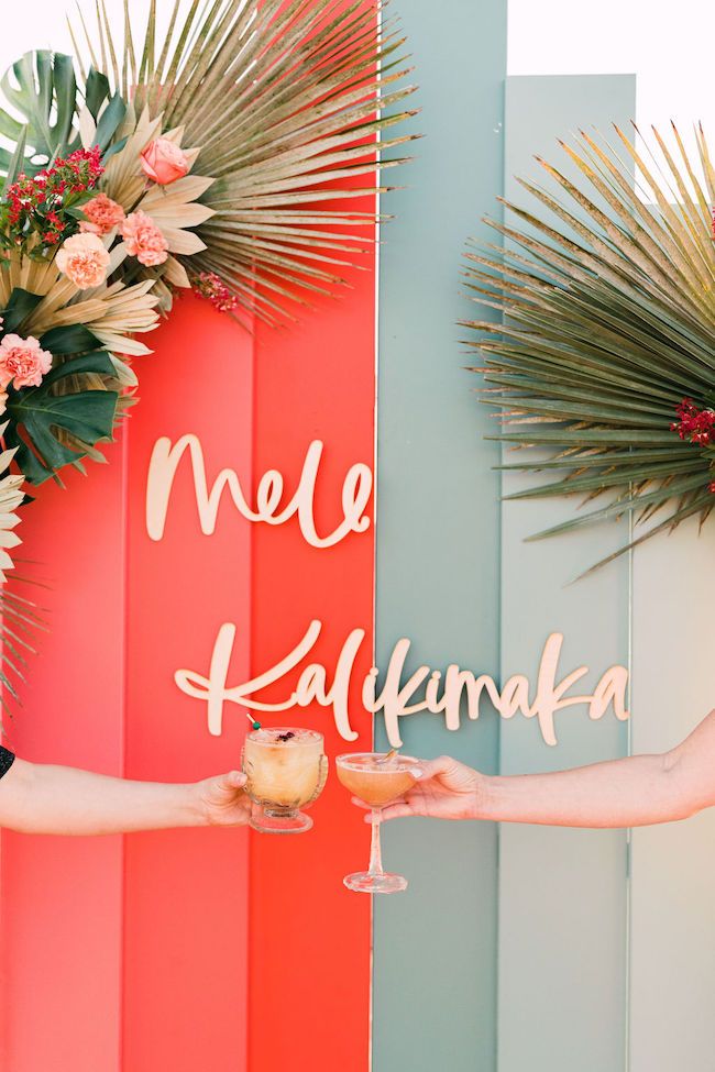 two people holding wine glasses in front of a colorful wall that says mele kaafmaka