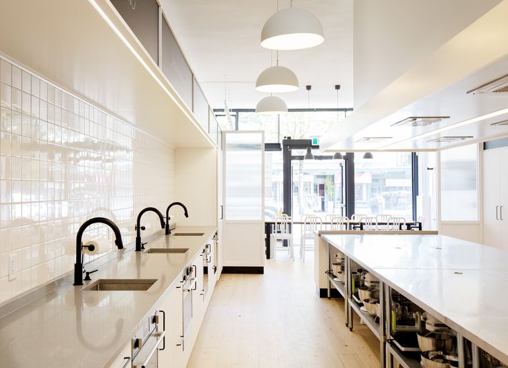 an empty kitchen with lots of counter space and hanging lights above the sink, along with white cabinets