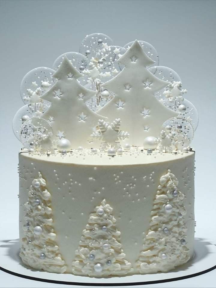 a white frosted christmas cake with trees and snowflakes on the top tier