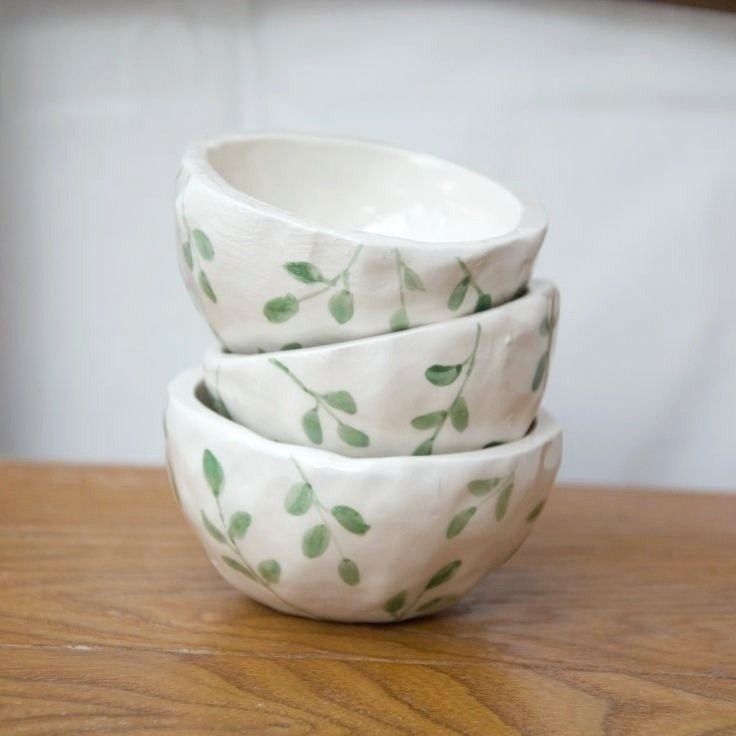 three white bowls stacked on top of each other with green leaves painted all over them